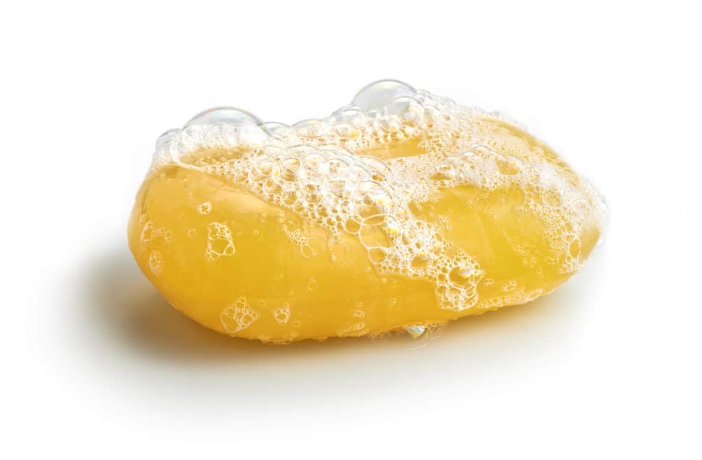 yellow soap bar with sudsy bubbles against white background