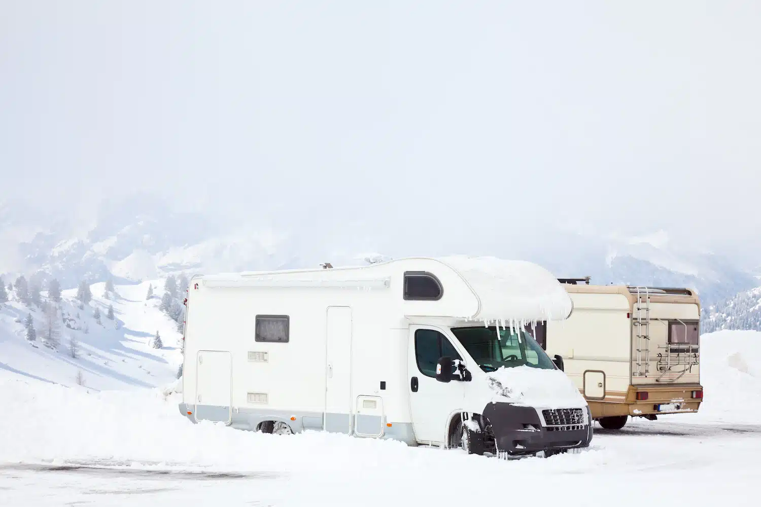 two RVs with ice hanging off of vehicle parked in snow near mountains