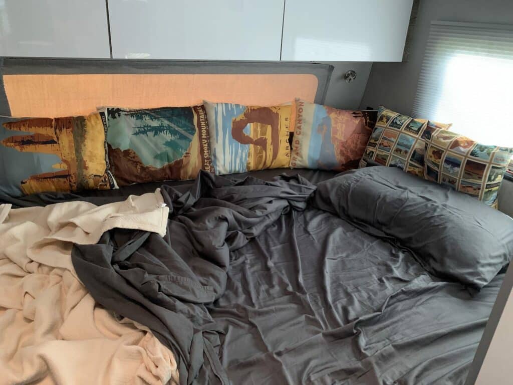 messy sheets on RV mattress with pillows propped up against walls