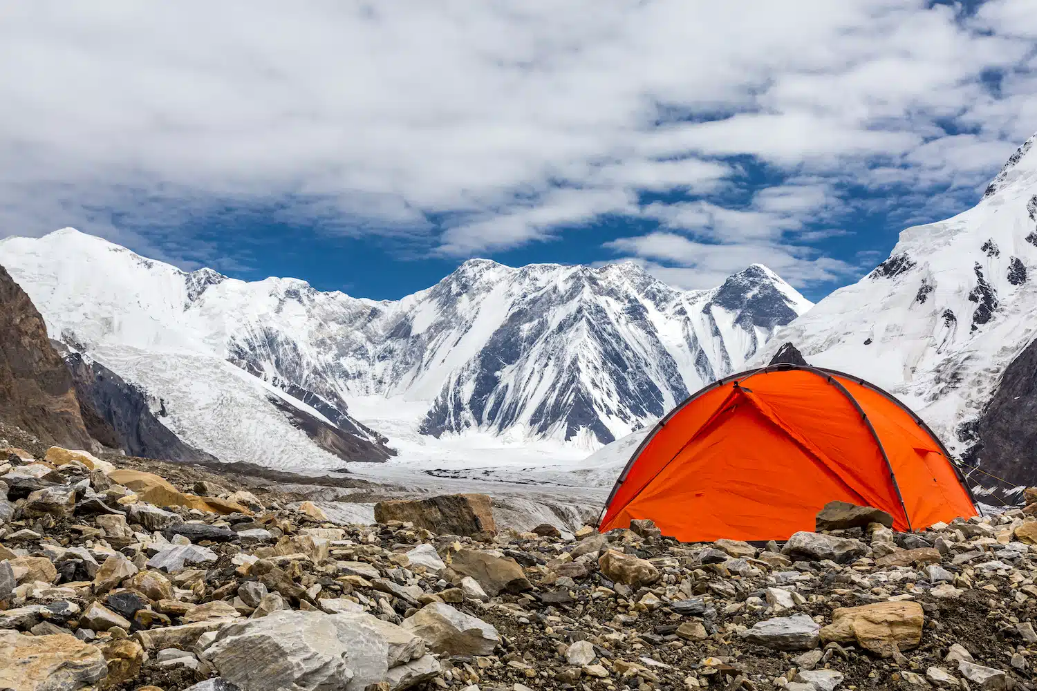 orange camping tent on rocky side of mountain with glaciers in distance