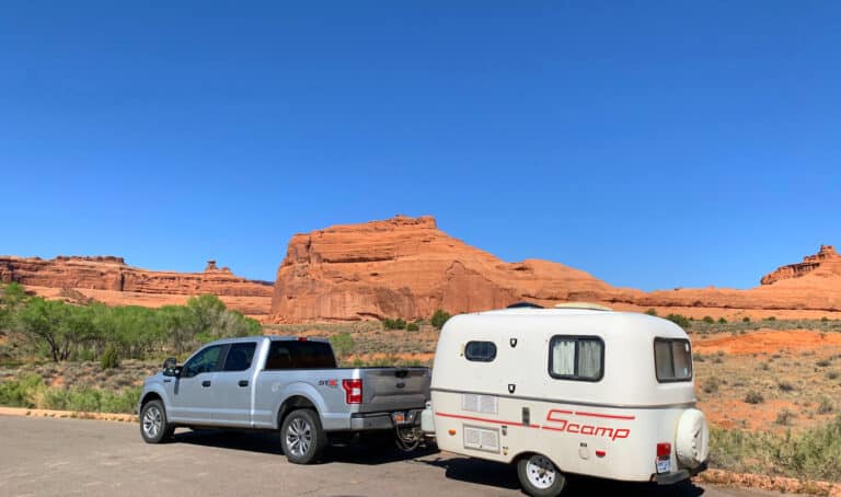truck towing a small lightweight trailer with red rock mountains in distance