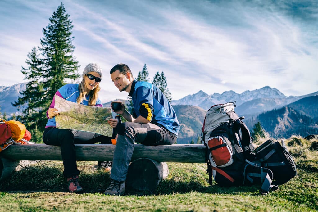 Couple hikers sitting on a bench with map atop a mountain
