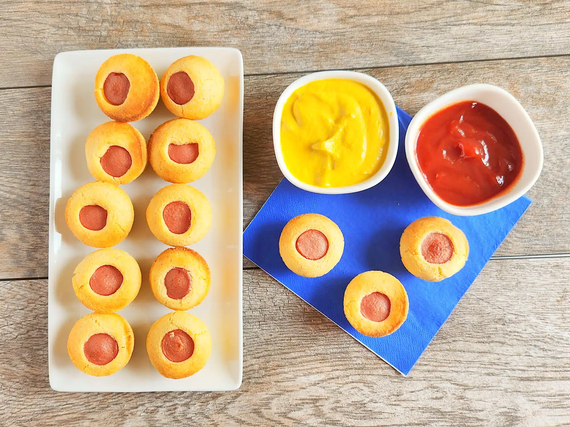 plate of corn dog muffins next to blue napkin and bowls of ketchup and mustard