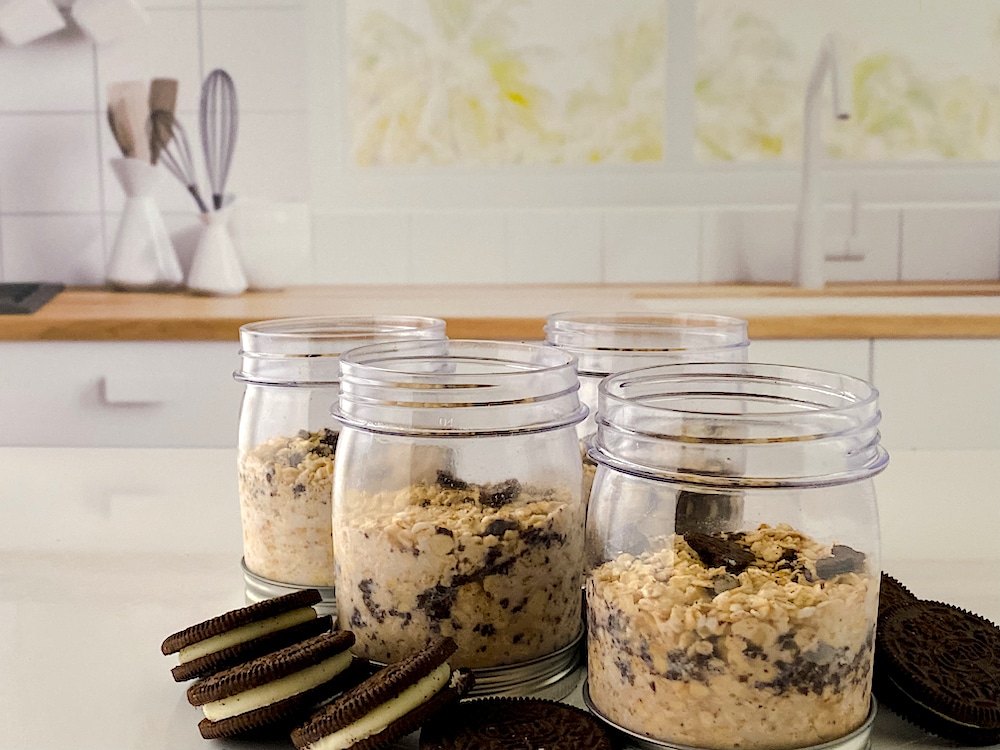 Cookies N Creme Overnight Oats in small jars with Oreo cookies on countertop