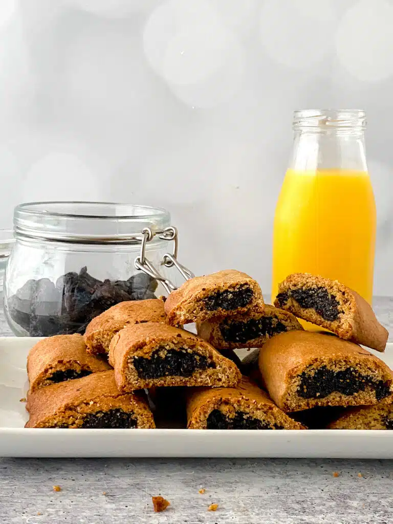Homemade Fig Newtons piled on a plate on the table with orange juice bottle in background