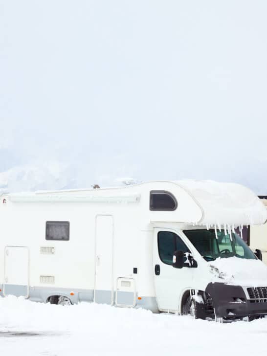 two RVs parked in a snowy field with mountains in distance