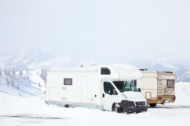 two RVs parked in a snowy field with mountains in distance
