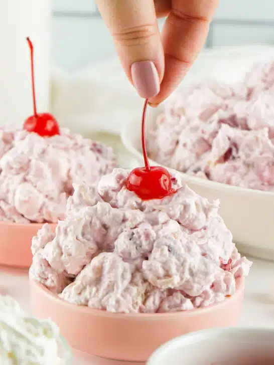 woman's hand putting a cherry with a stem on top of cherry fluff salad in bowls