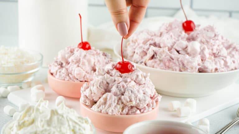 woman's hand putting a cherry with a stem on top of cherry fluff salad in bowls