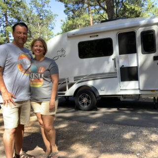 man and woman standing together in front of a small teardrop RV