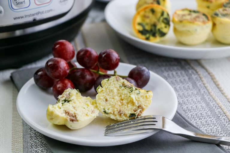 small sous vide egg bites on a white plate with red grapes and a fork in front of an Instant Pot