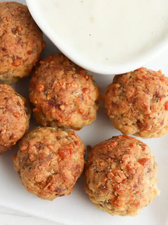 breakfast sausage meatballs on a white serving tray with a bowl of homemade gravy next to blue and white checkered towel