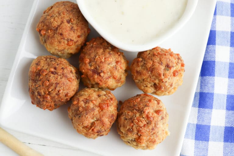 breakfast sausage meatballs on a white serving tray with a bowl of homemade gravy next to blue and white checkered towel