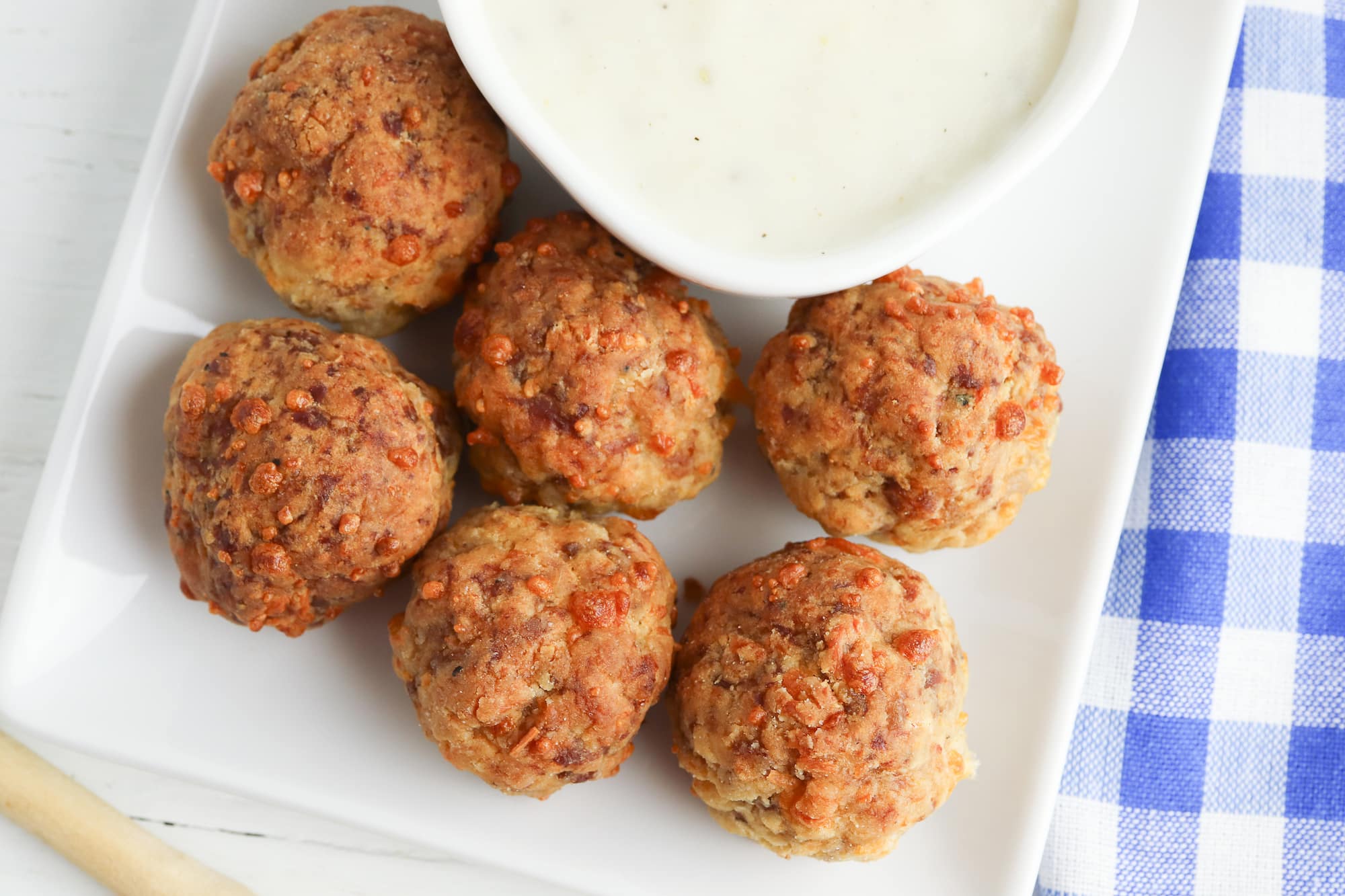 breakfast sausage meatballs on a white serving tray with a bowl of homemade gravy next to blue and white checkered towel