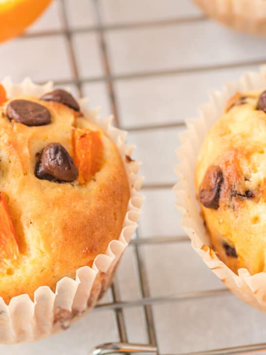 orange chocolate chip muffins laying on wire cooling rack on marble countertop