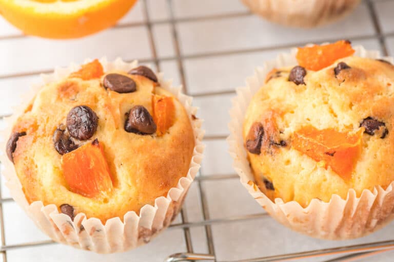 orange chocolate chip muffins laying on wire cooling rack on marble countertop