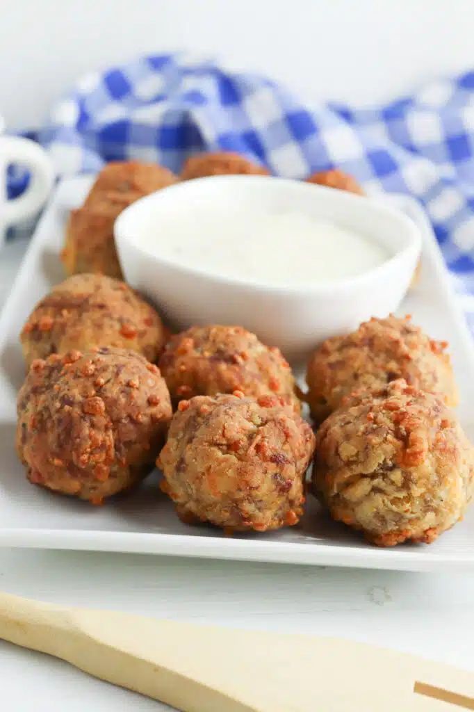 baked breakfast meatballs on white platter with small bowl filled with gravy and blue and white checkered towel in background