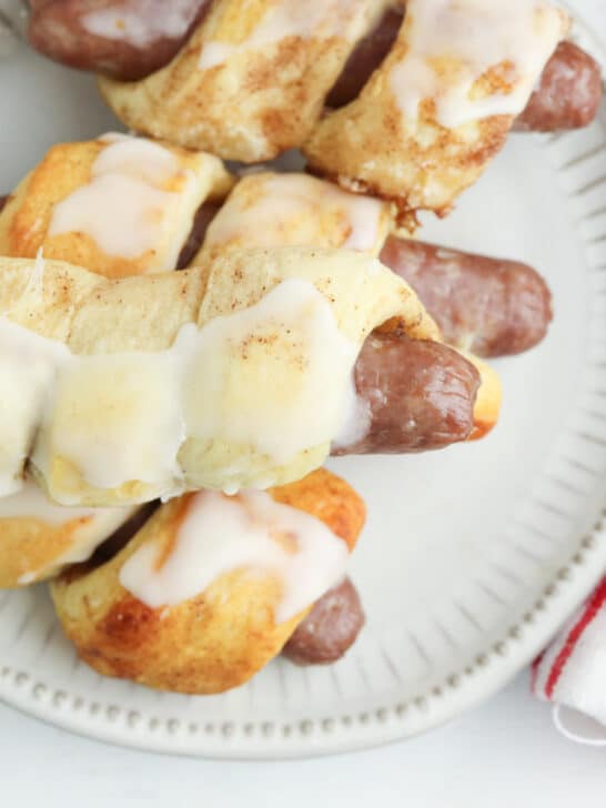cinnamon roll pigs in a blanket stacked on a plate with a red and white plaid towel nearby