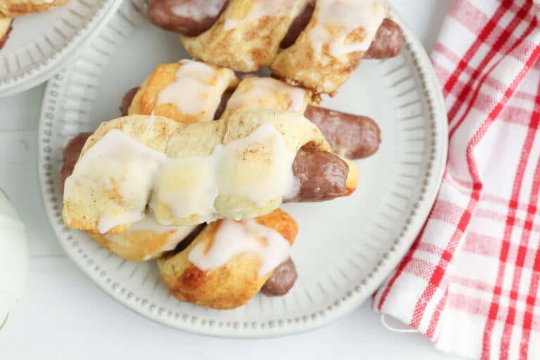 cinnamon roll pigs in a blanket stacked on a plate with a red and white plaid towel nearby