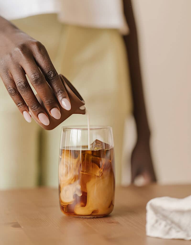 ice coffee drink with dark skinned person pouring cream into beverage