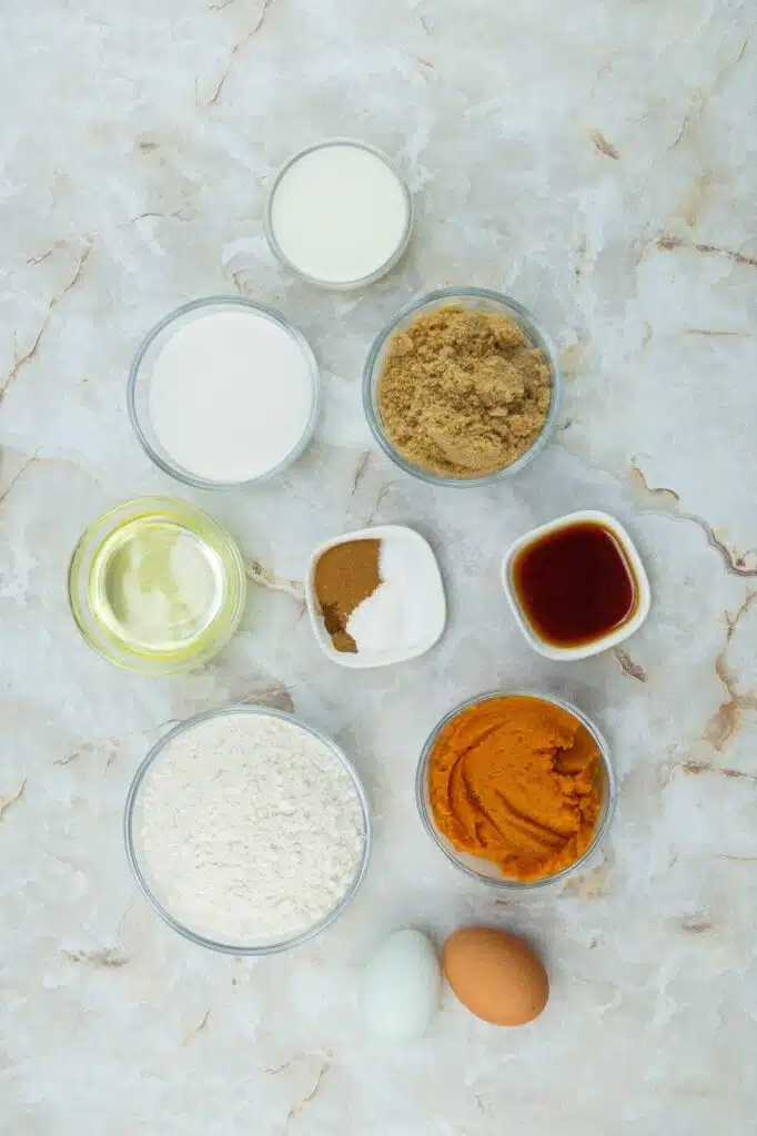 Ingredients for a pumpkin pie recipe on a marble surface.