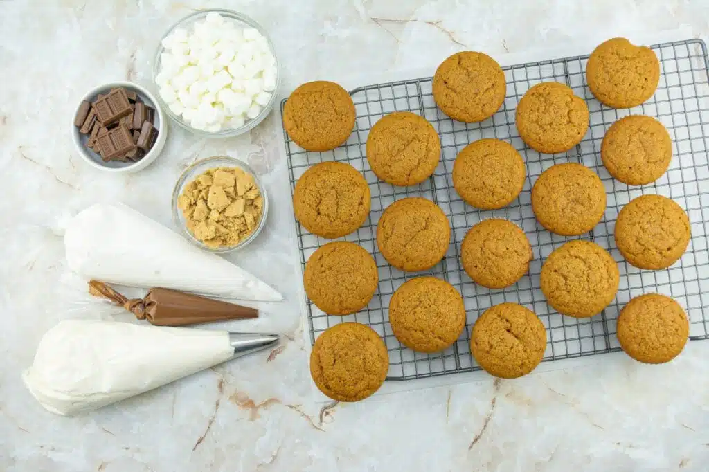 Pumpkin cookies on a cooling rack with chocolate chips and marshmallows.