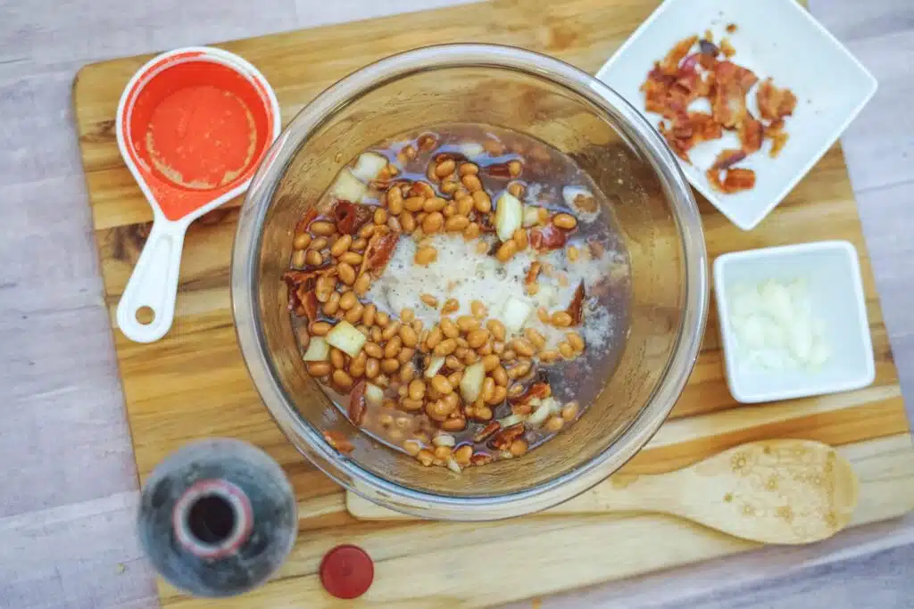 A bowl of beans and ingredients on a wooden cutting board.