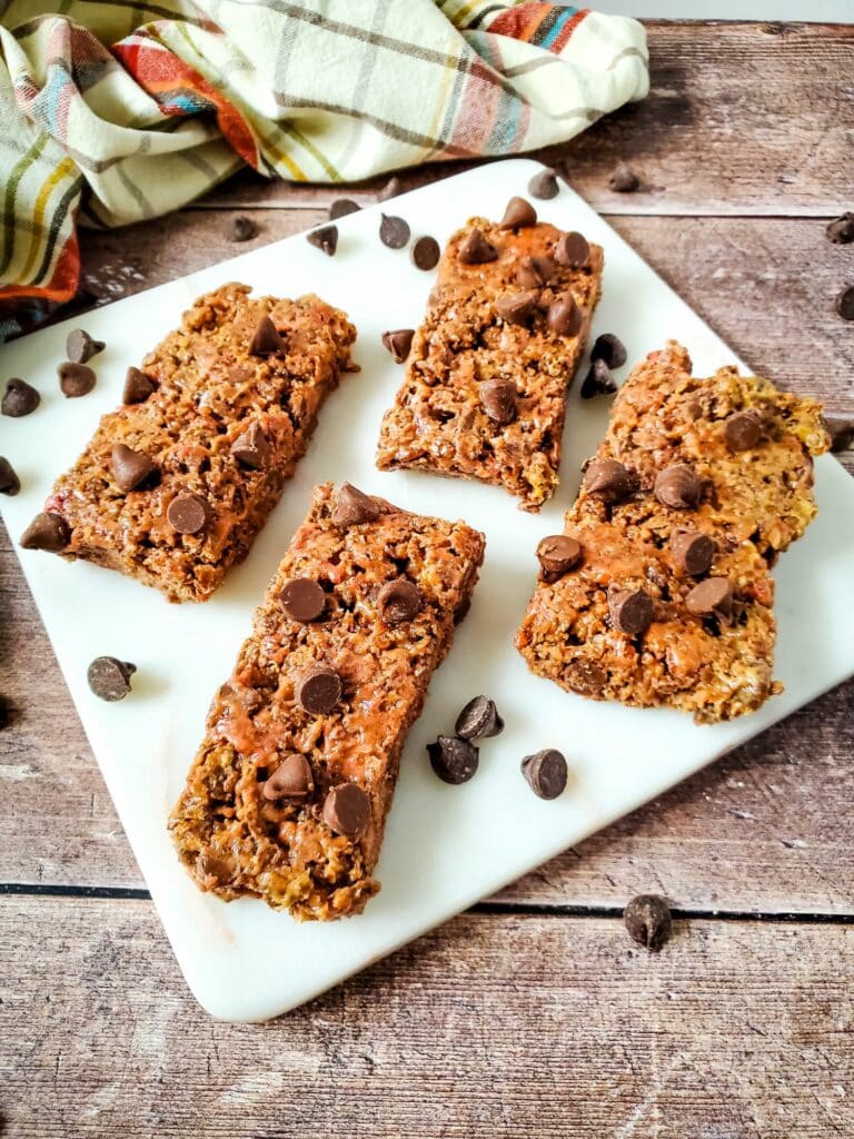 Four granola bars on a white plate with chocolate chips.