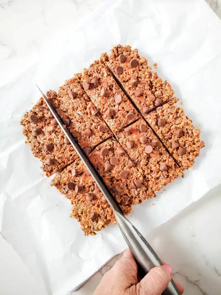 A person cutting granola bars with a knife.