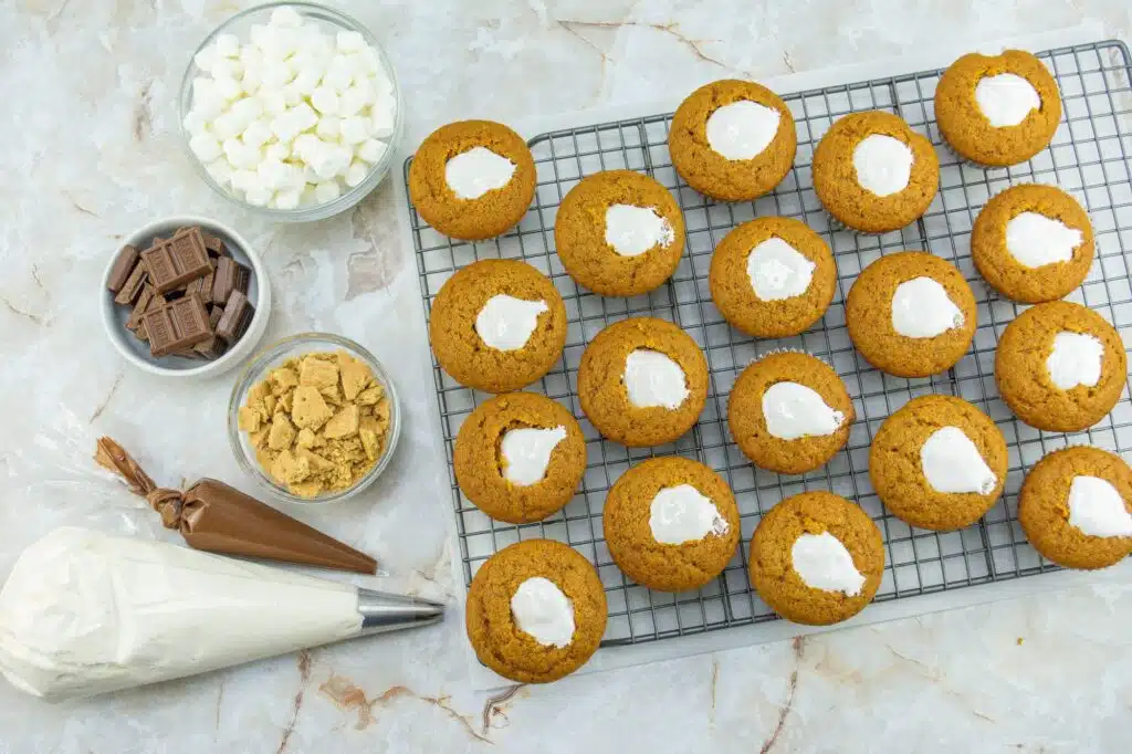 Pumpkin cookies on a cooling rack with whipped cream and chocolate chips.