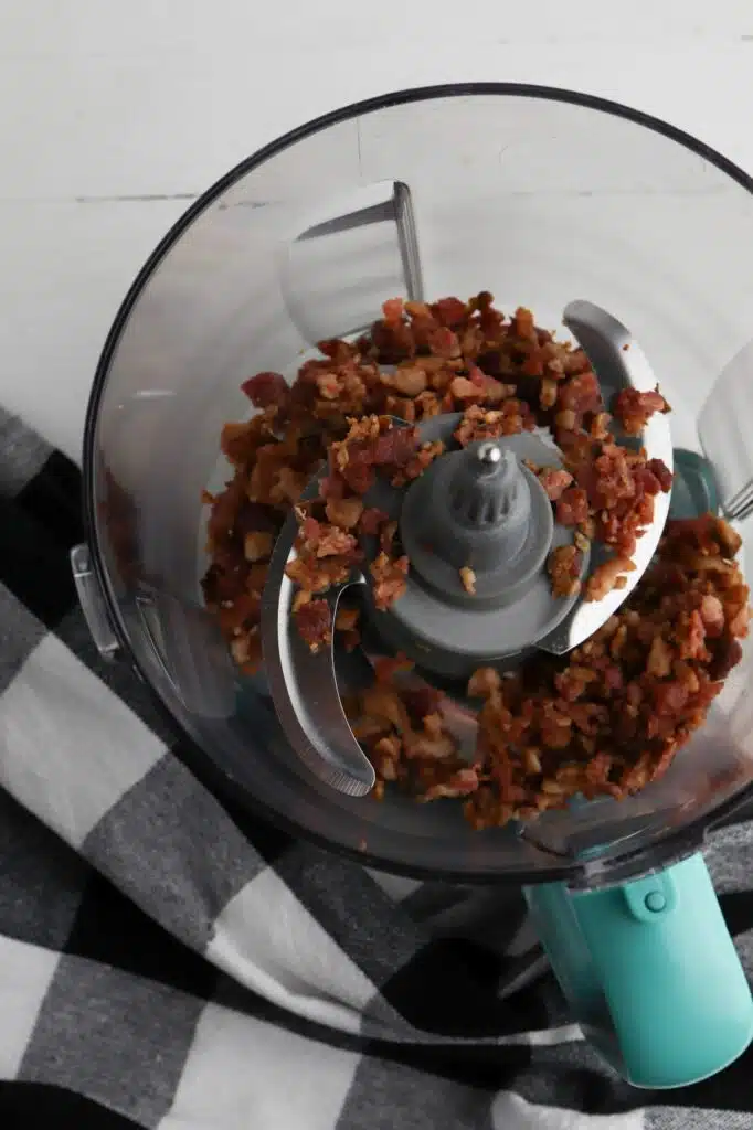 Bacon in a food processor on a checkered tablecloth.