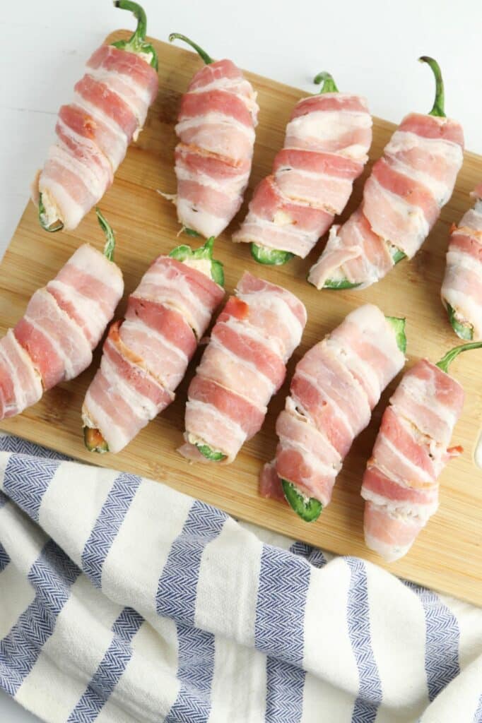 Bacon wrapped peppers on a cutting board.