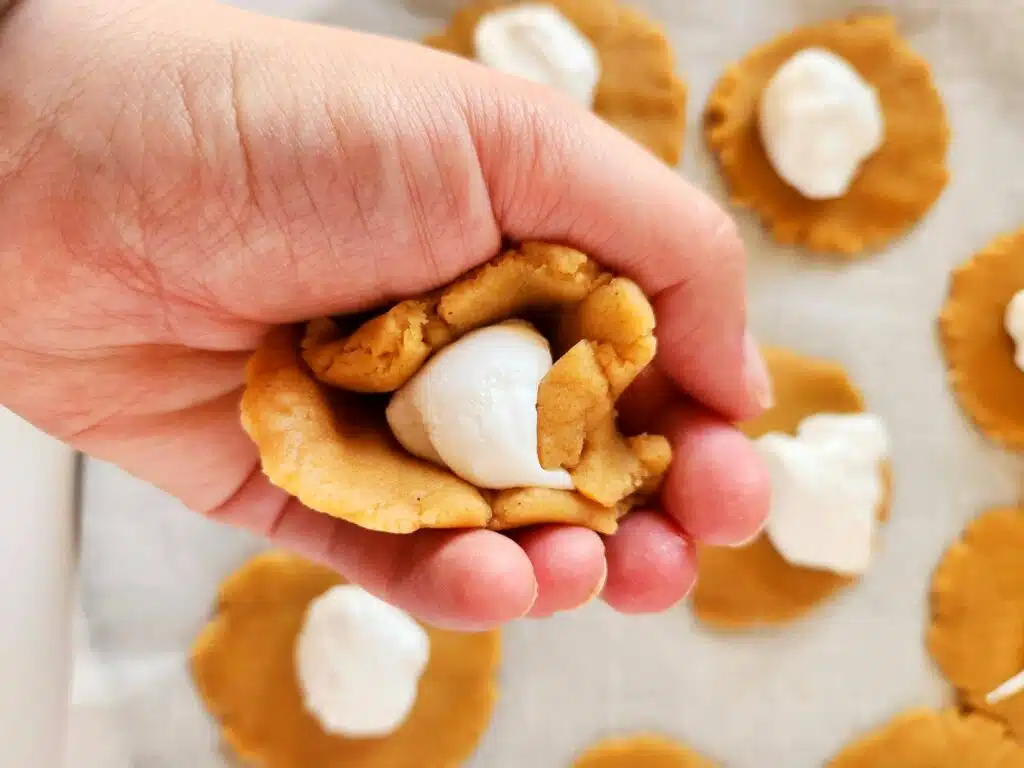 A hand is holding a cookie with whipped cream on it.