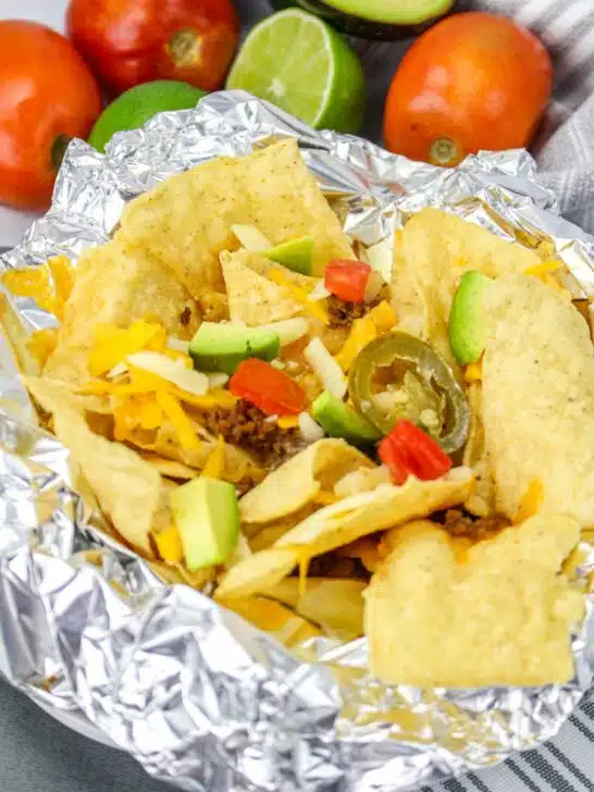 A plate of nachos in foil with tomatoes and avocados.