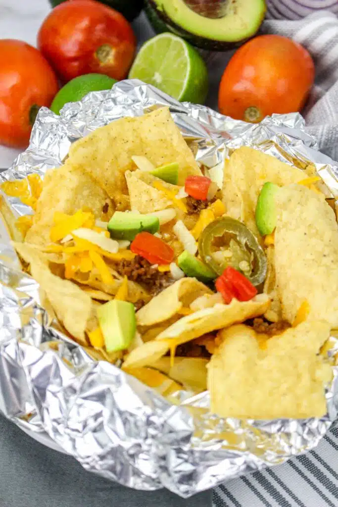 A plate of nachos in foil with tomatoes and avocados.