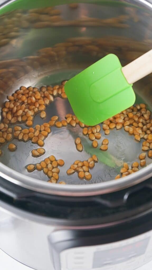 A green spatula is being used to stir beans in an instant pot.