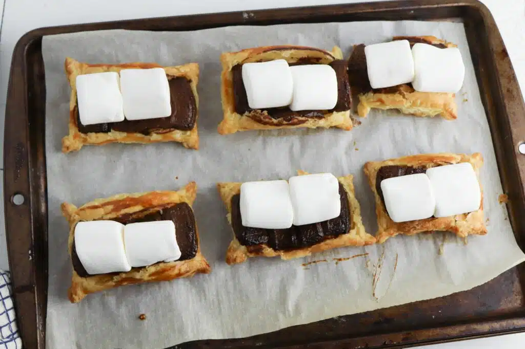 S'mores tarts on a baking sheet with marshmallows.