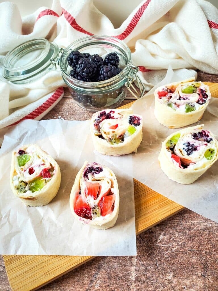 A tray of fruit and berry tarts on a cutting board.