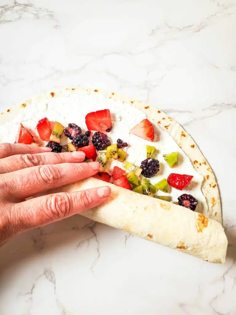 A hand is holding a tortilla with fruit on it.