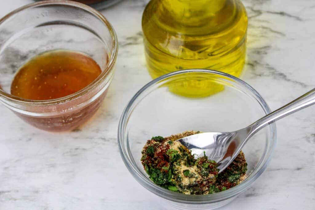 A glass with a spoon and a bottle of olive oil next to it.