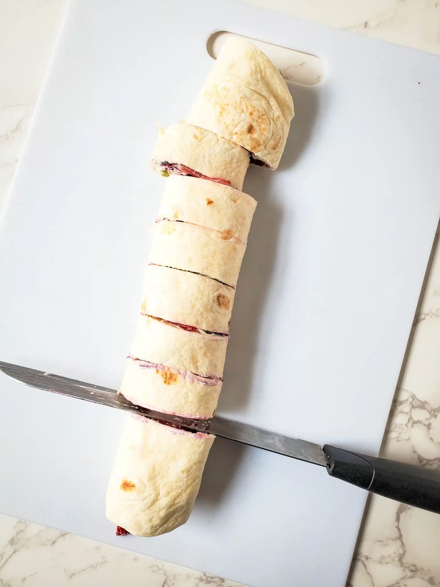 A burrito on a cutting board with a knife.