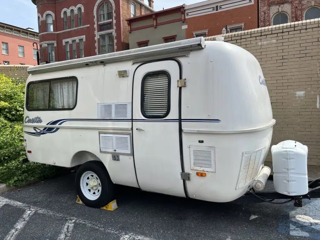 A small white camper trailer parked in a parking lot, perfect for those seeking the best fiberglass campers with bathrooms.