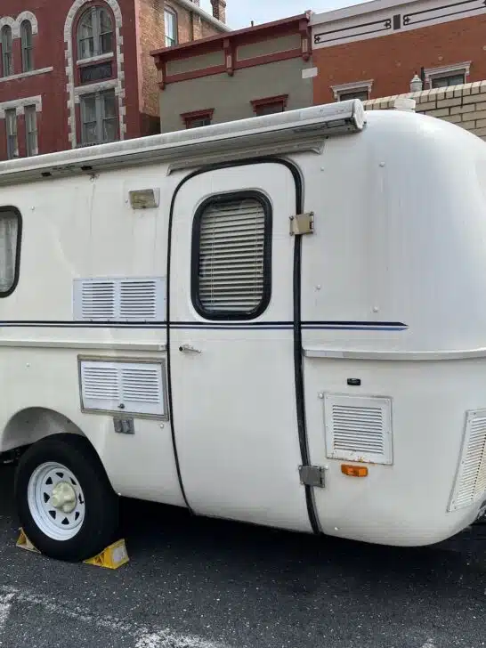 A small white camper trailer parked in a parking lot, perfect for those seeking the best fiberglass campers with bathrooms.