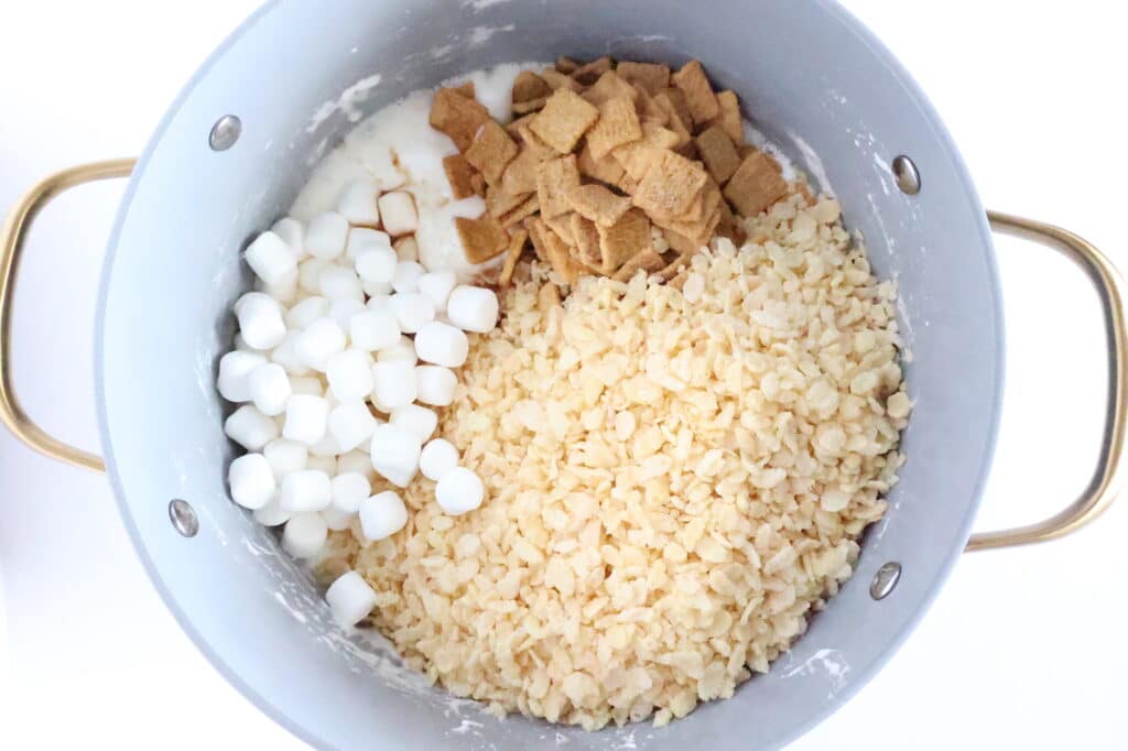 A pot containing mini marshmallows, cereal squares, and rice crisps on a white background.