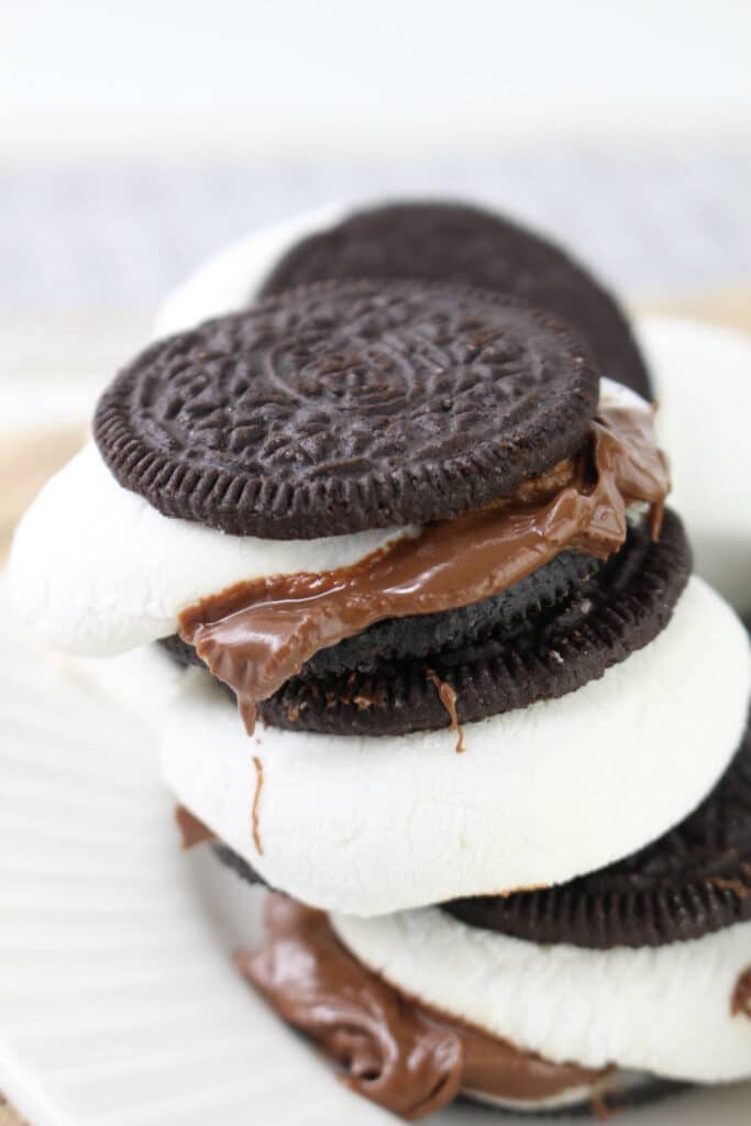 Stack of sandwich cookies with marshmallow and chocolate filling on a white plate.