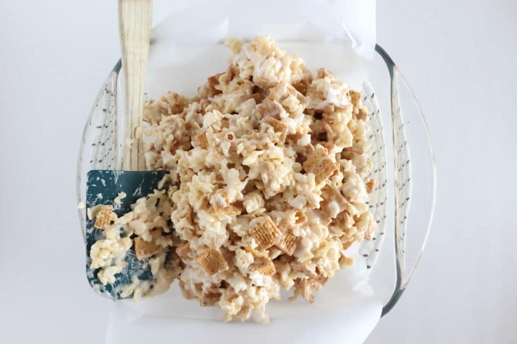 A glass dish filled with cereal and marshmallow mixture, with a spatula on the side.