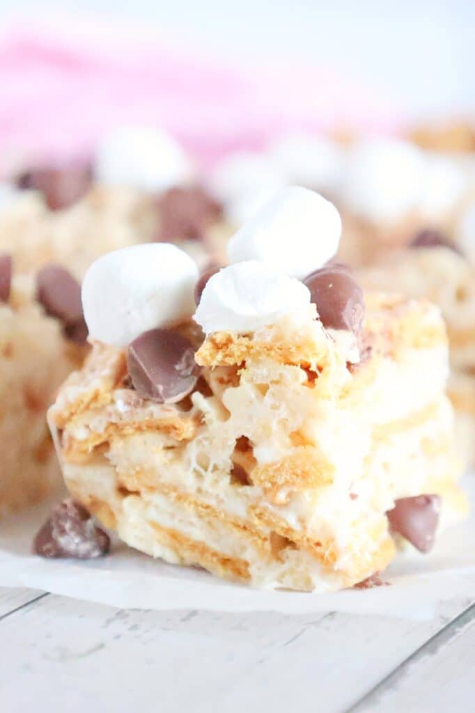 Close-up of a dessert bar with layers of graham crackers, topped with chocolate chips and mini marshmallows on a white surface.