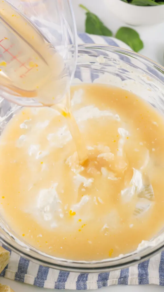 Pouring liquid into a bowl containing a mixture of cream and yellow sauce on a striped cloth.