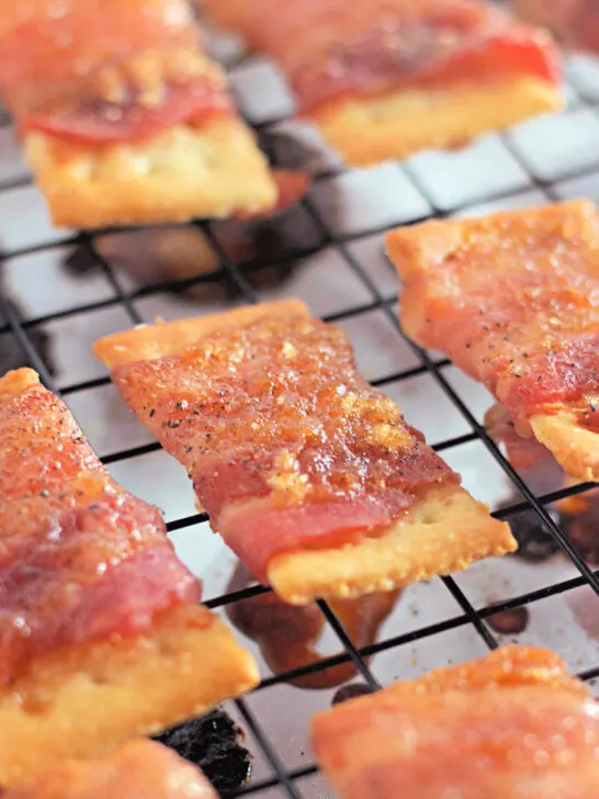 Close-up of bacon-wrapped crackers on a cooling rack, each sprinkled with seasoning, demonstrating a freshly baked snack.