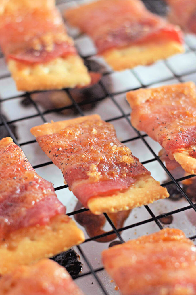 Close-up of bacon-wrapped crackers on a cooling rack, each sprinkled with seasoning, demonstrating a freshly baked snack.